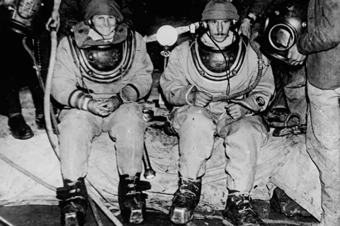 Penelope Powell and Graham Balcombe kitted up in Wookey Hole Cave for the first ever cave dive in 1935. Historical photo courtesy of Mendip Cave Registry and Archive Cave Diving Group.
